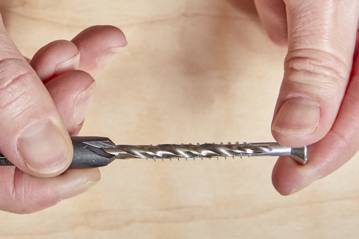 A person holds a drill bit between their fingers.