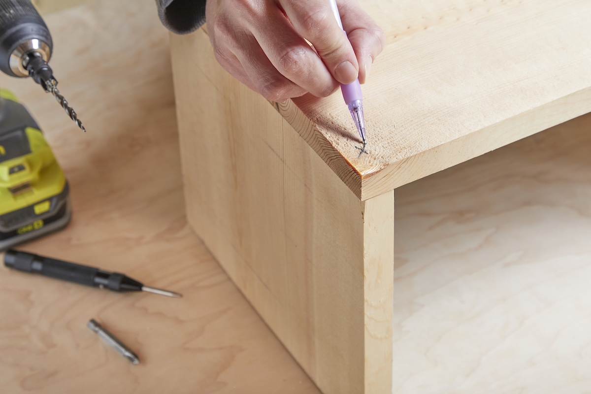A woman marks pieces of wood together "X" Where the pilot hall will go.