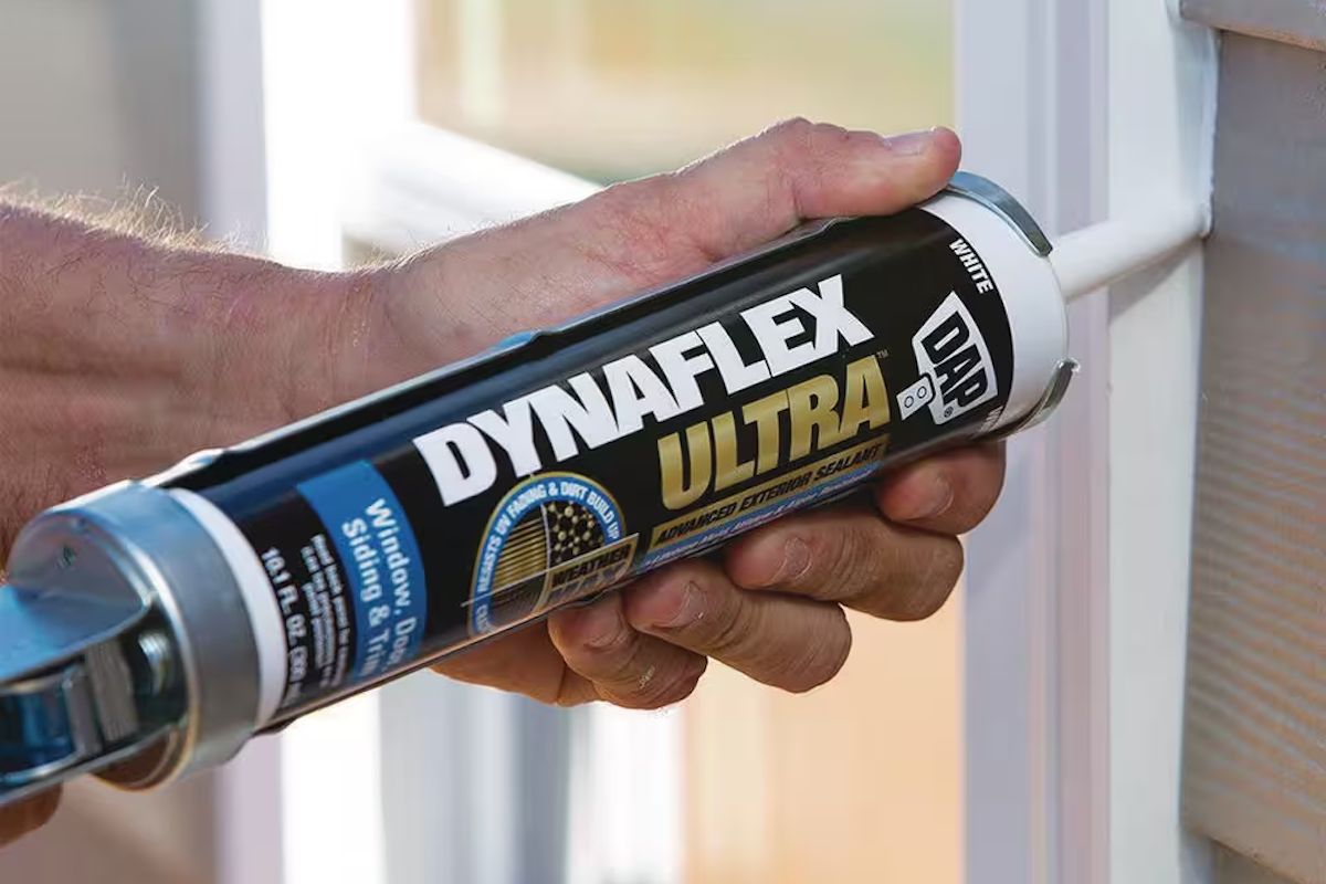 A person is using a caulking gun between an exterior window and fiber cement siding.