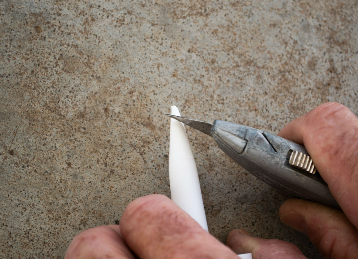 A person is cutting the tip off of a caulking gun with a utility knife.