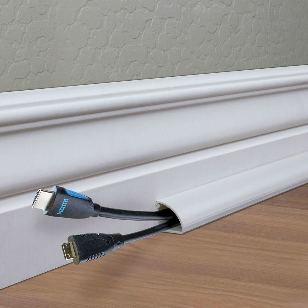 Computer cords hidden in a cord keeper along a white baseboard.