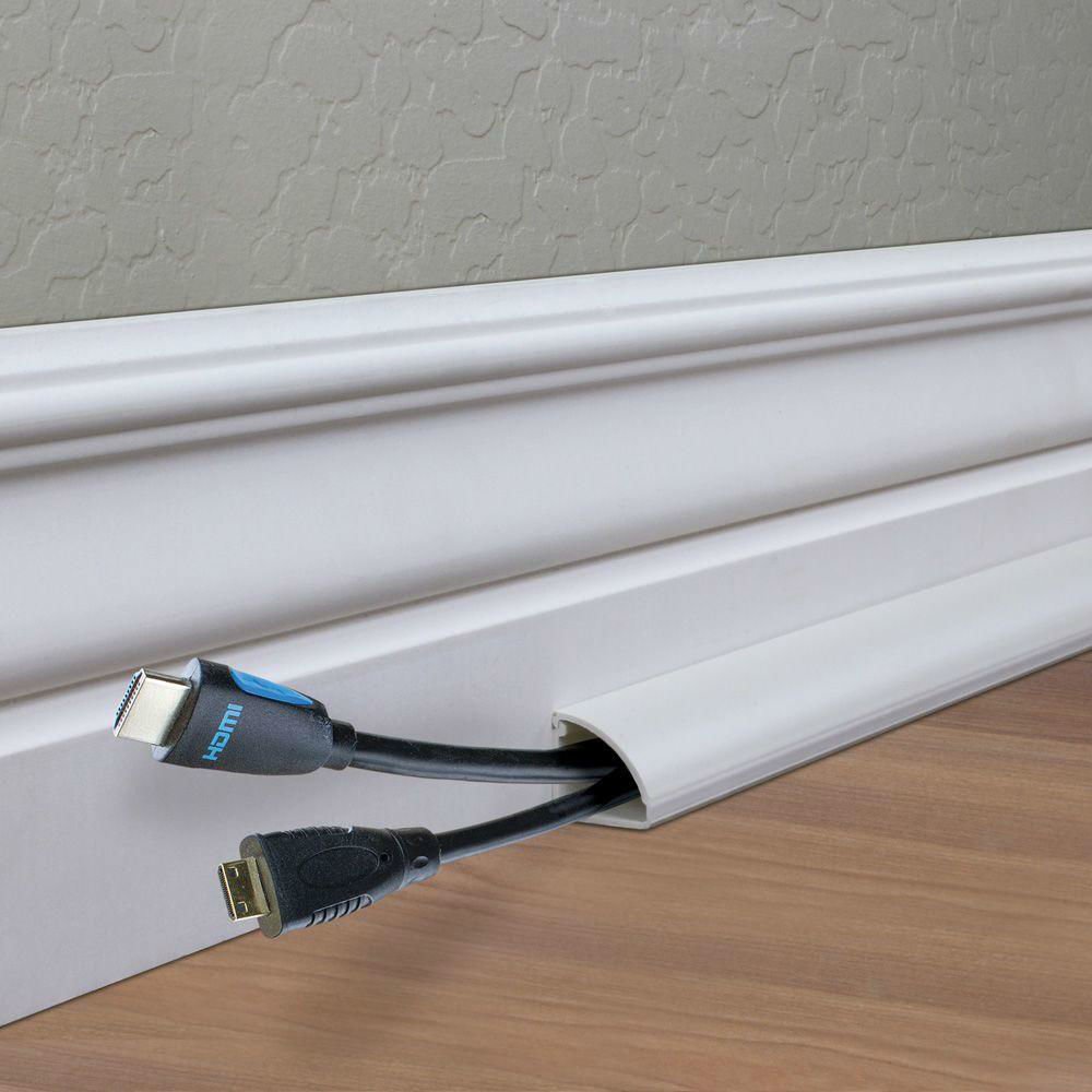Two lightning cords peeking out of a white baseboard cord channel on top of hardwood flooring.