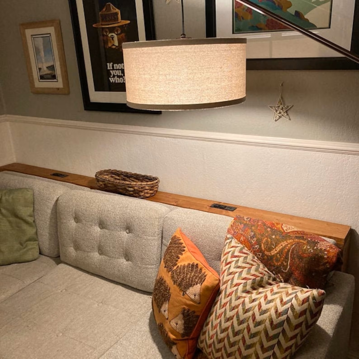 Slim wood sofa table behind a beige couch, with a round pendant light hanging overhead and artwork on the walls behind the sofa.