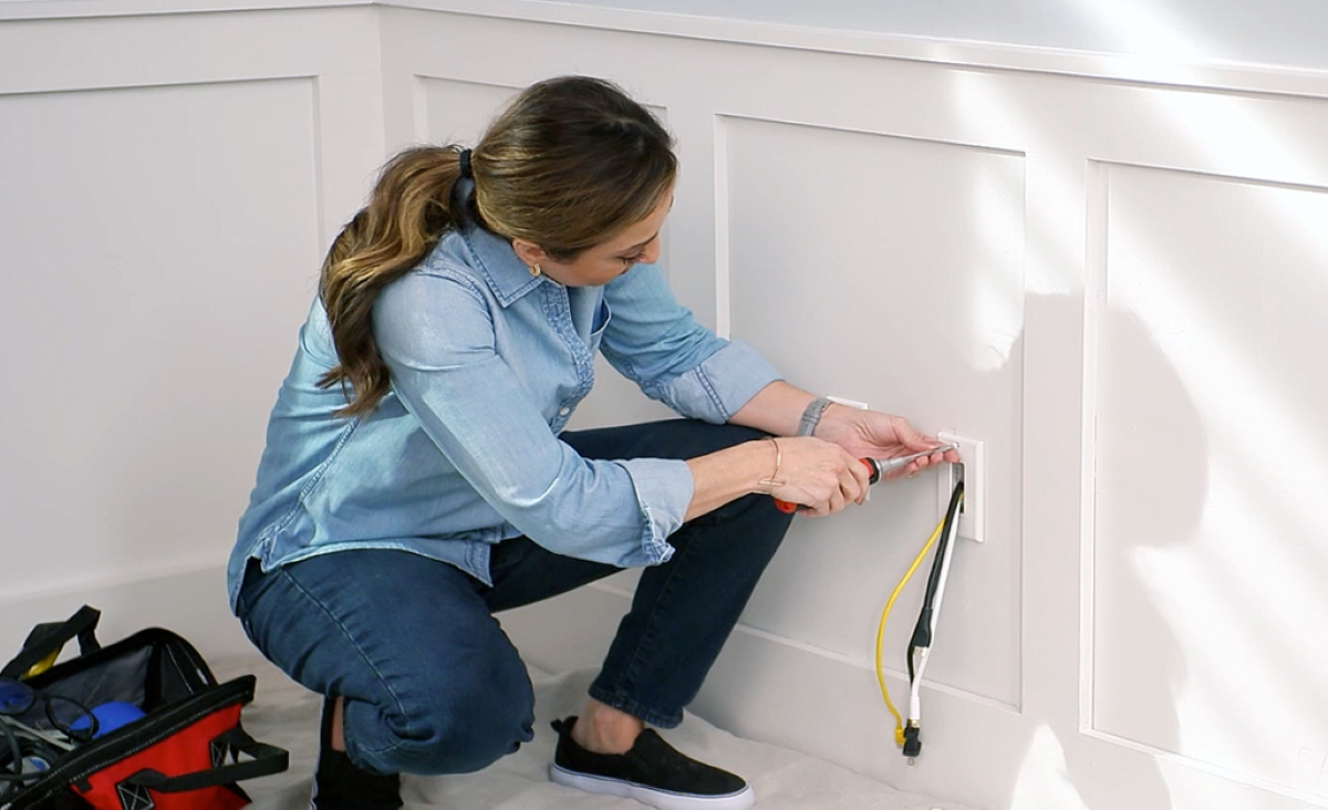 Woman hiding wires inside white wainscoted wall using a PVC conduit.