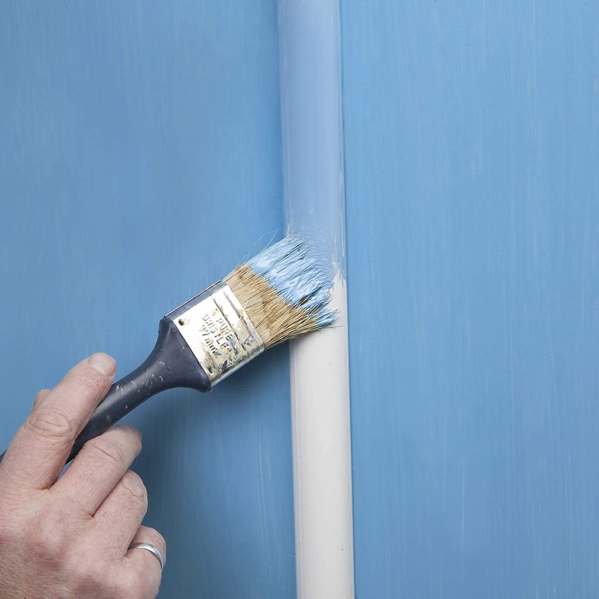 Person paints a white cable raceway light blue to match the light blue wall paint.