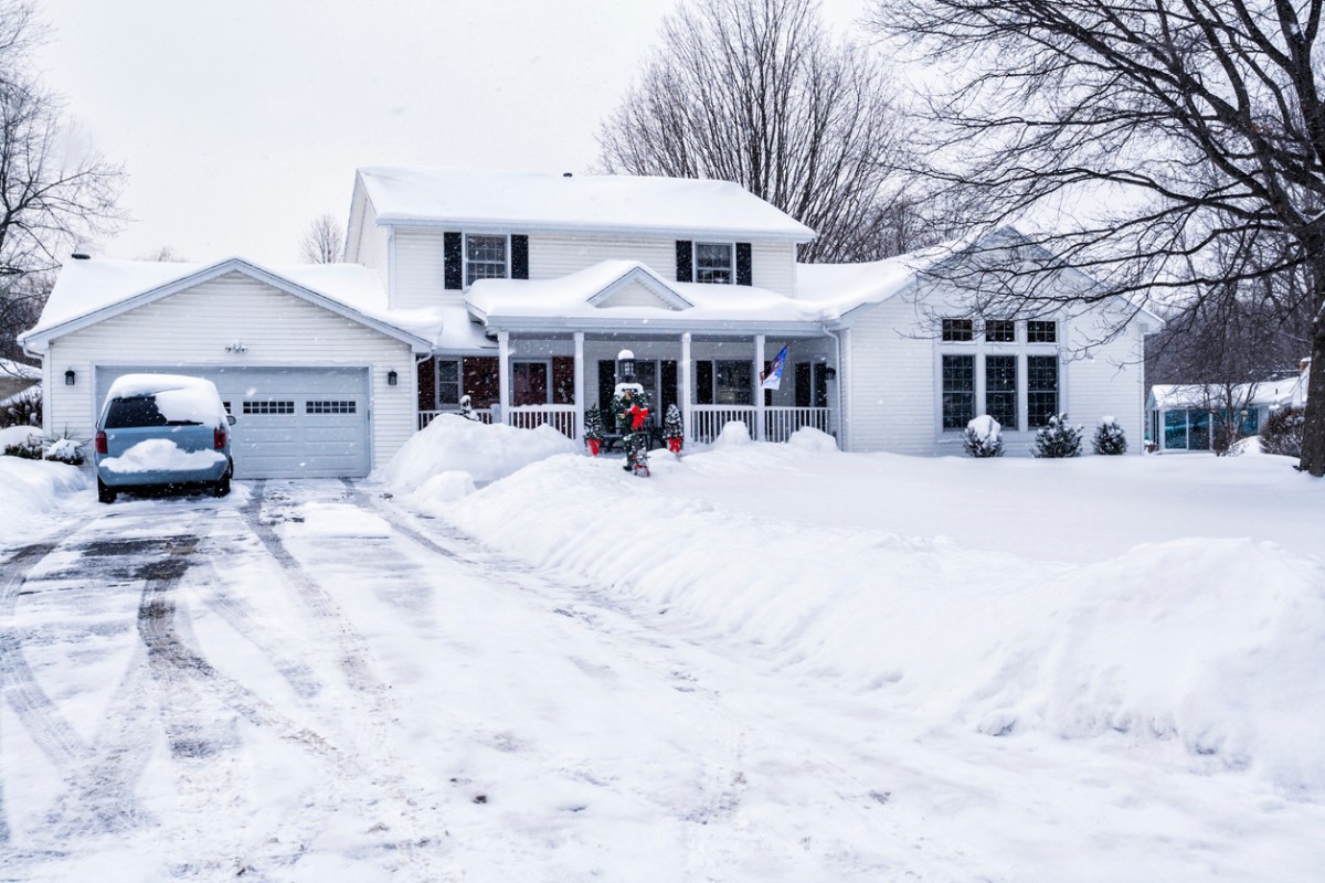 White home with porch and Christmas decorations with snow-covered driveway.
