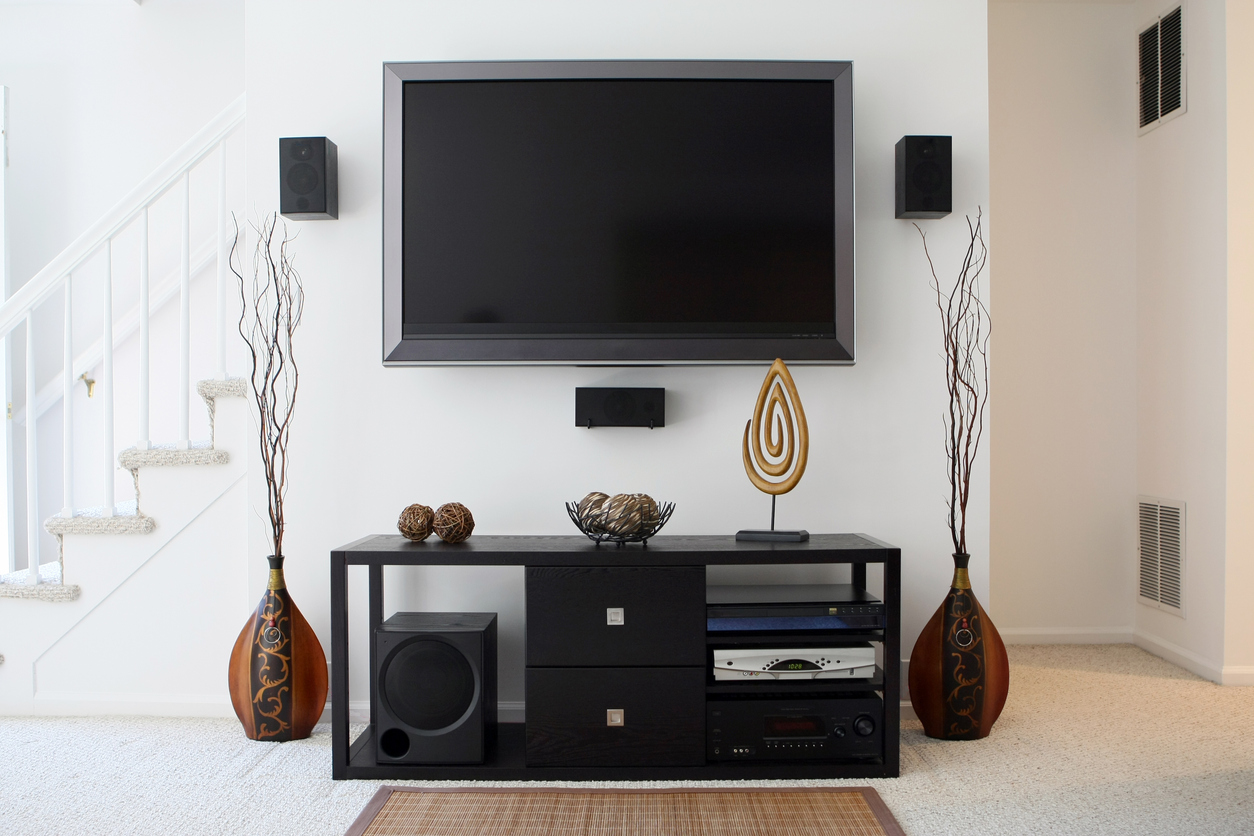 TV hangs on wall with stairs to the left, and a TV stand with modern wood sculptures and statues surrounding it.