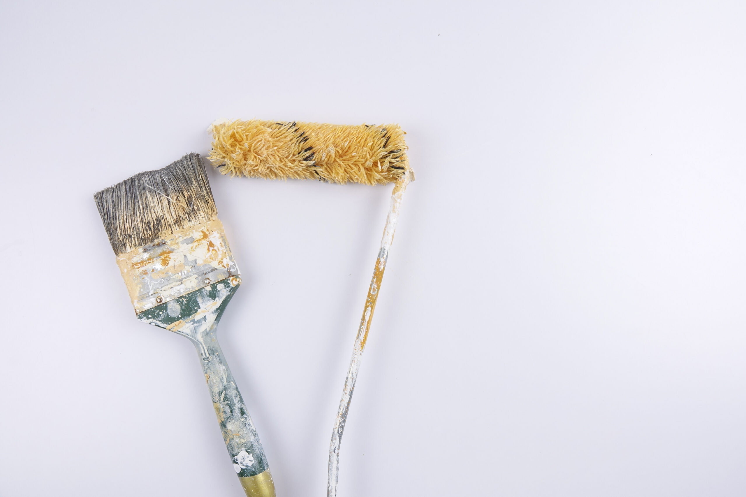 Dirty home paintbrush and paint roller in front of white backdrop.