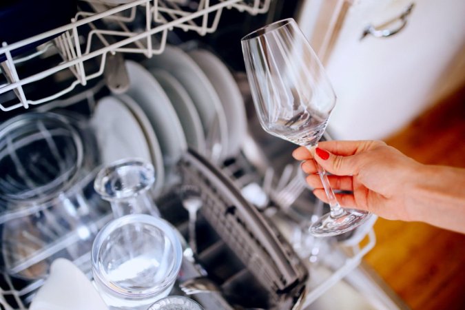 Woman holds a wine glass over a full dishwasher.