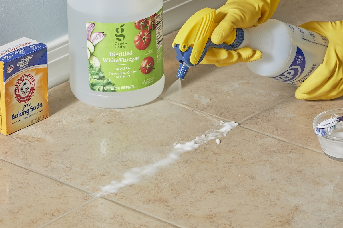 Person sprays grout with vinegar-baking soda mixture.
