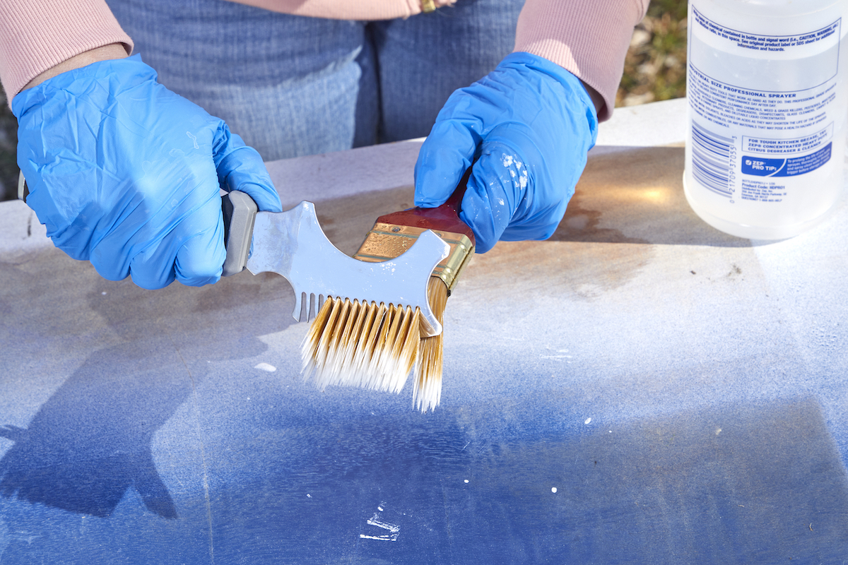 Woman uses a paint multitool to clean and straighten the bristles of a paintbrush.