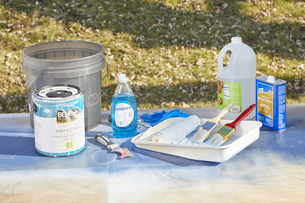 Painting and cleaning supplies on a table outdoors, including paint tray, bucket, soap, and vinegar.