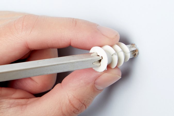 Close up view of a woman holding a drywall anchor between her fingers, with a screwdriver in the anchor.