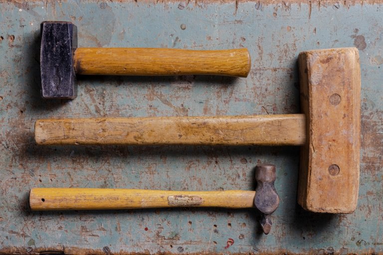 Three different types of hammers on a worn work table.