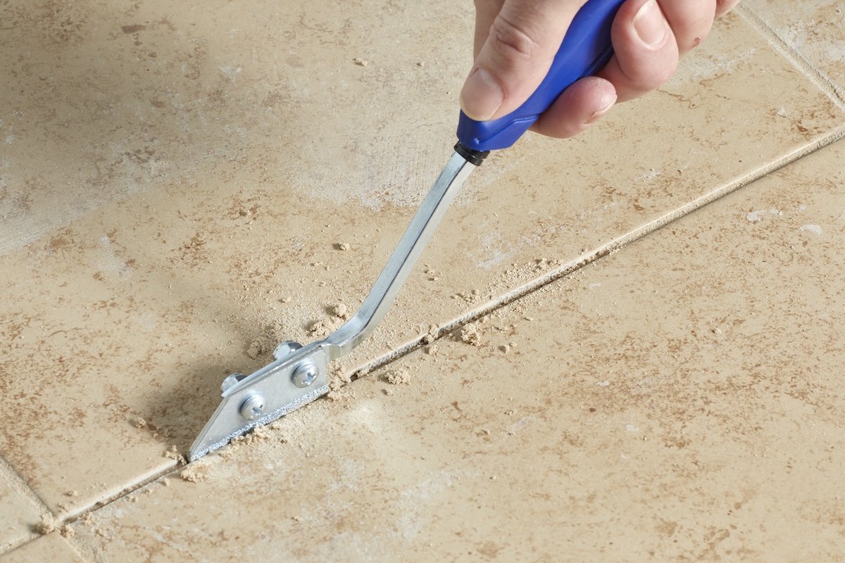 Someone uses a grout saw to remove the grout from tiled bathroom floors. 