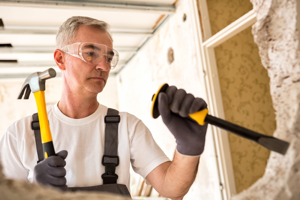 A man wearing eye protection and gloves while using a hammer. 