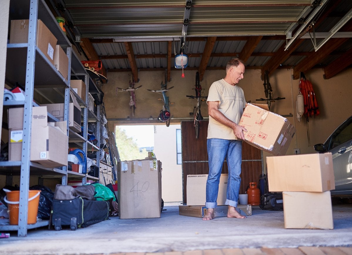 A man in the garage holding a cardboard box.