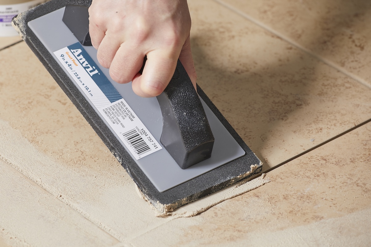 Person uses grout float to press grout between tiles on floor.
