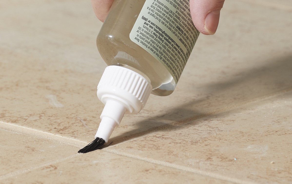 Person applies grout sealer to grout between beige tiles.
