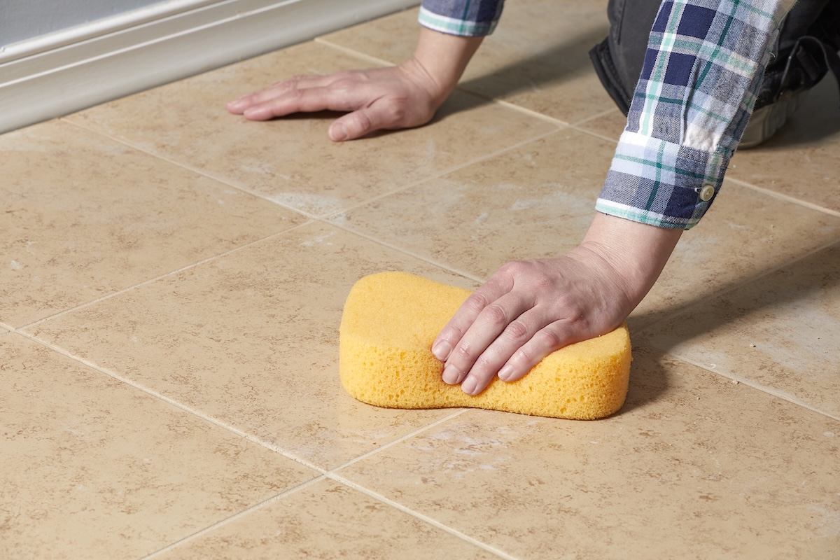 Person uses grout sponge to wipe grout off floor tile.