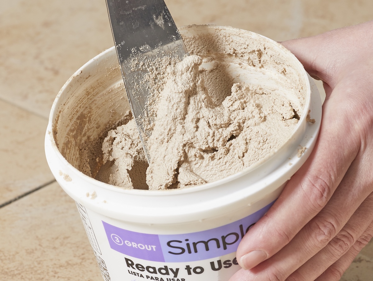Person using a metal putty knife to stir ready-to-use tile grout.