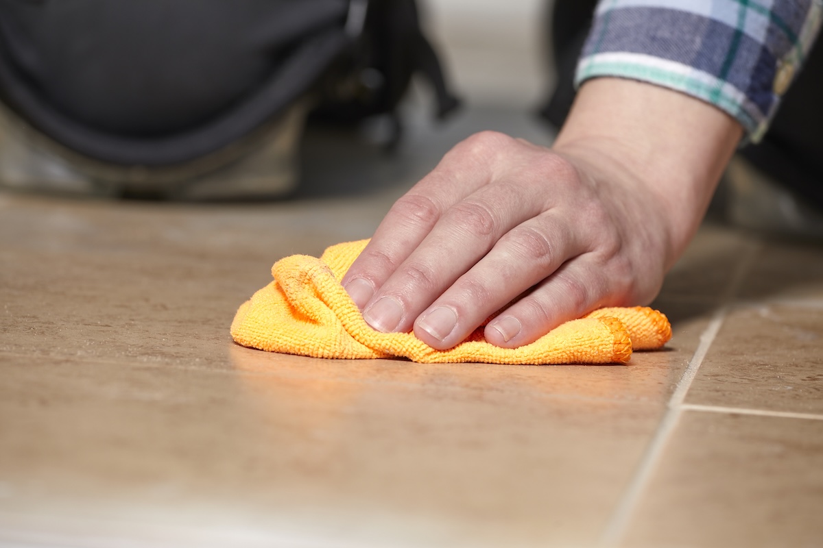 Woman wipes tile floor with yellow microfiber towel.