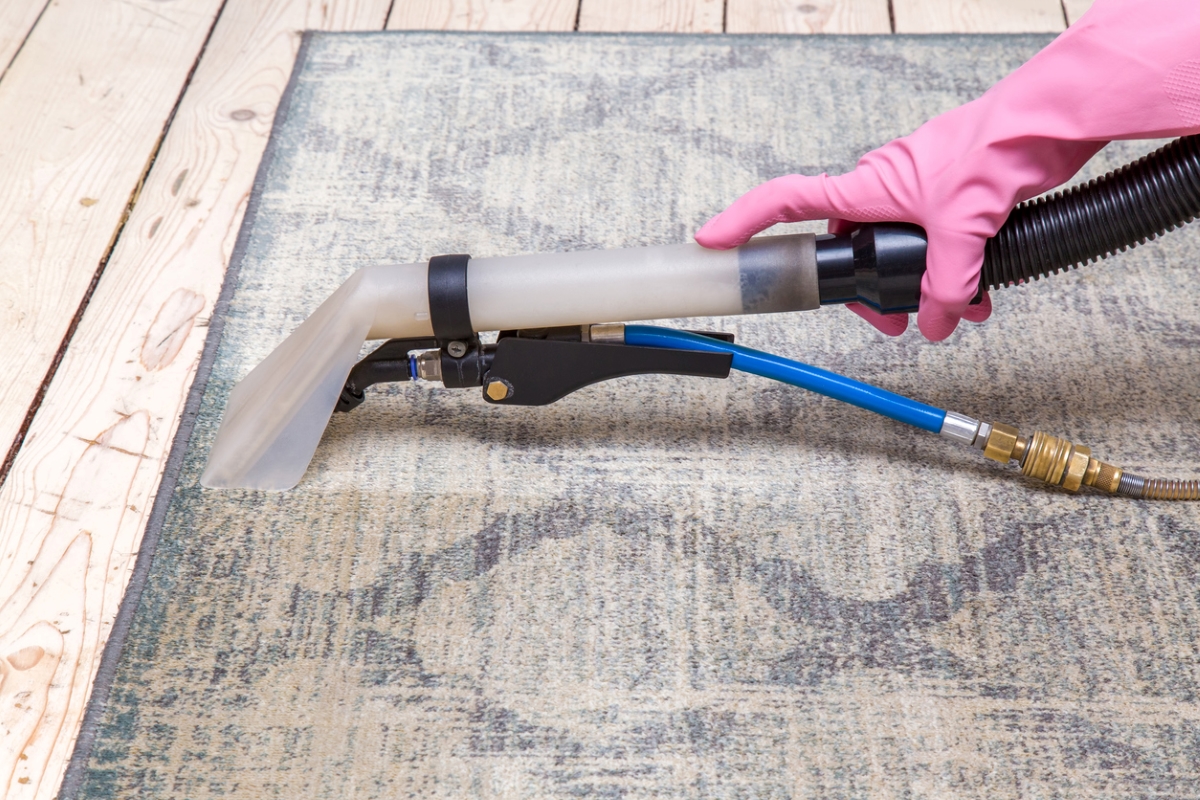 A gloved hand using vacuum to clean outdoor rug.
