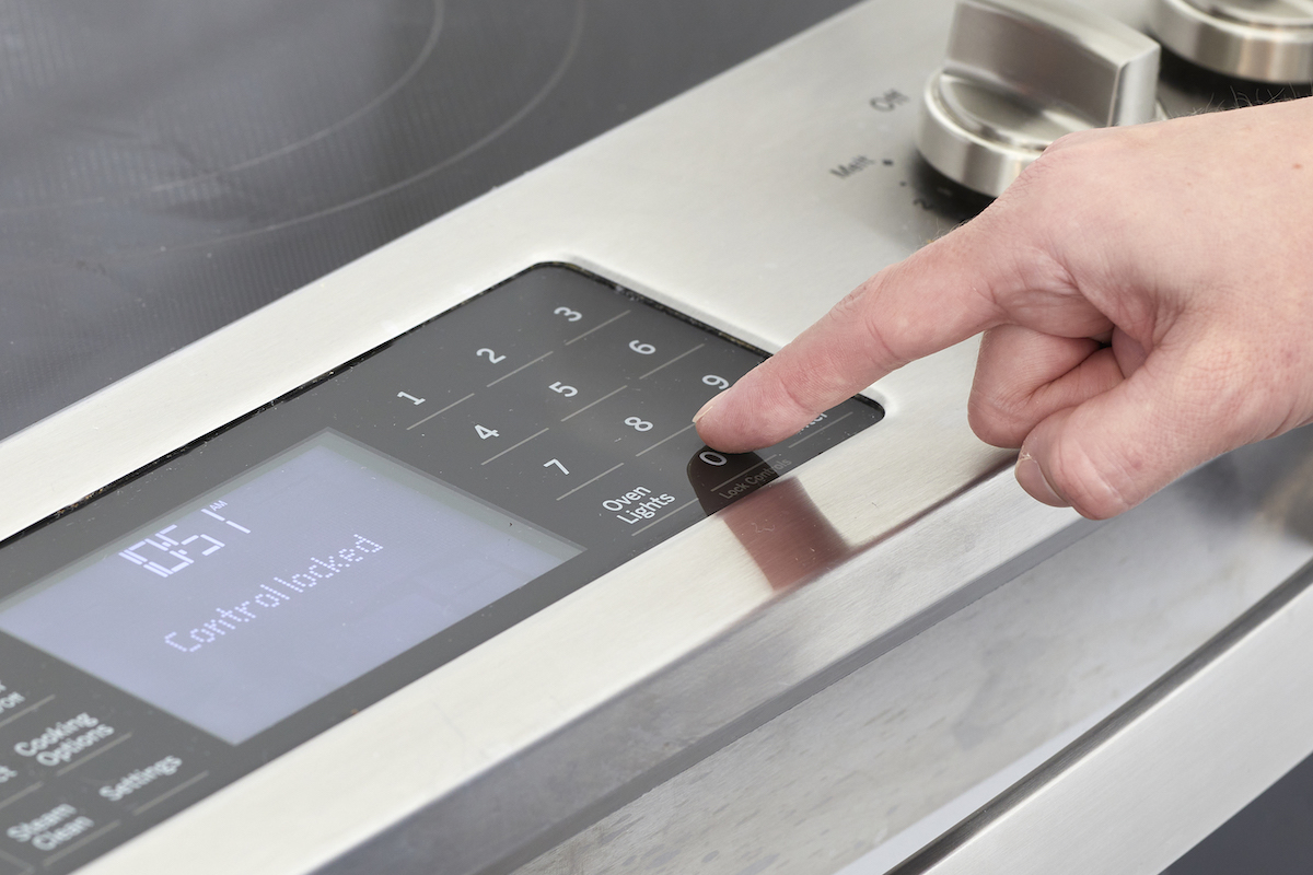 Digital screen on oven reads "control locked"; woman presses button to unlock it.