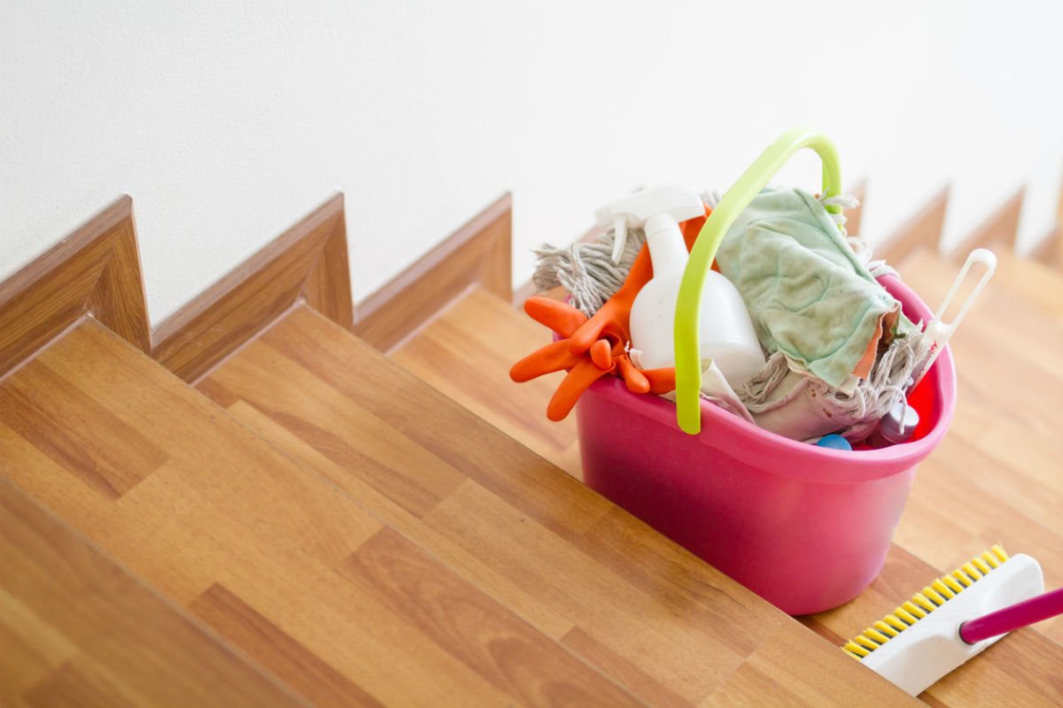 A bucket of cleaning supplies, including the best hardwood floor cleaner option, sits on a set of hardwood stairs