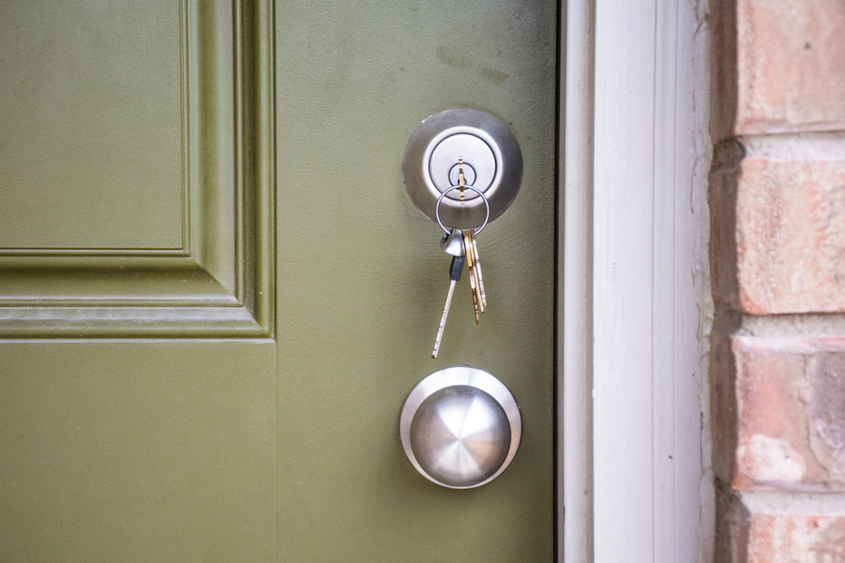 A green door to a brick home with a pair of keys hanging from a lock.