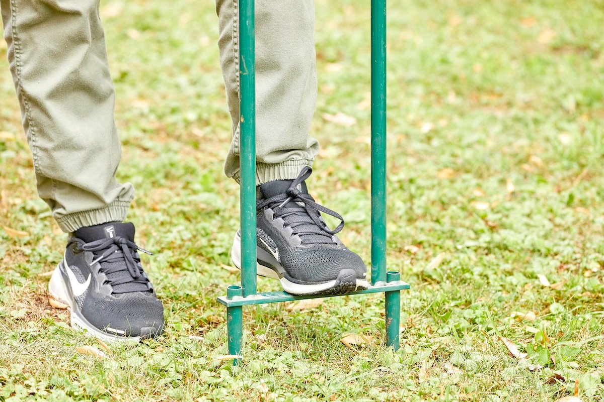 View of woman's pushing with one sneakered foot onto a manual yard aerator.
