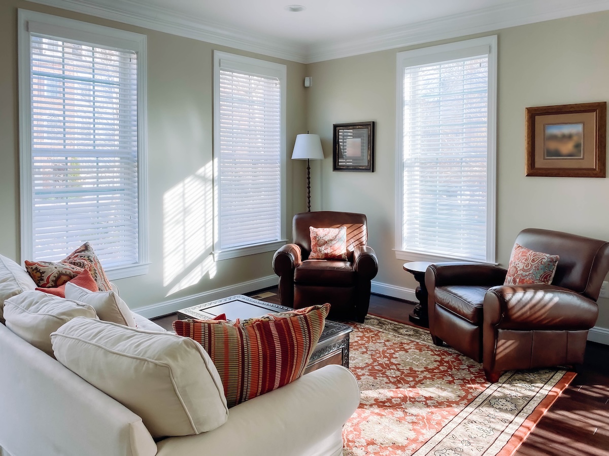 Horizontal blinds on the windows of a comfortable living room with a couch and chairs.
