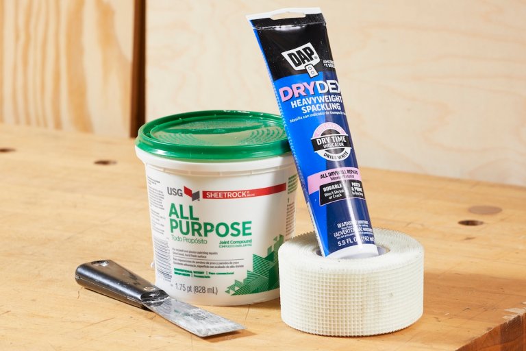 Containers of joint compound and spackle with a putty knife and drywall tape.