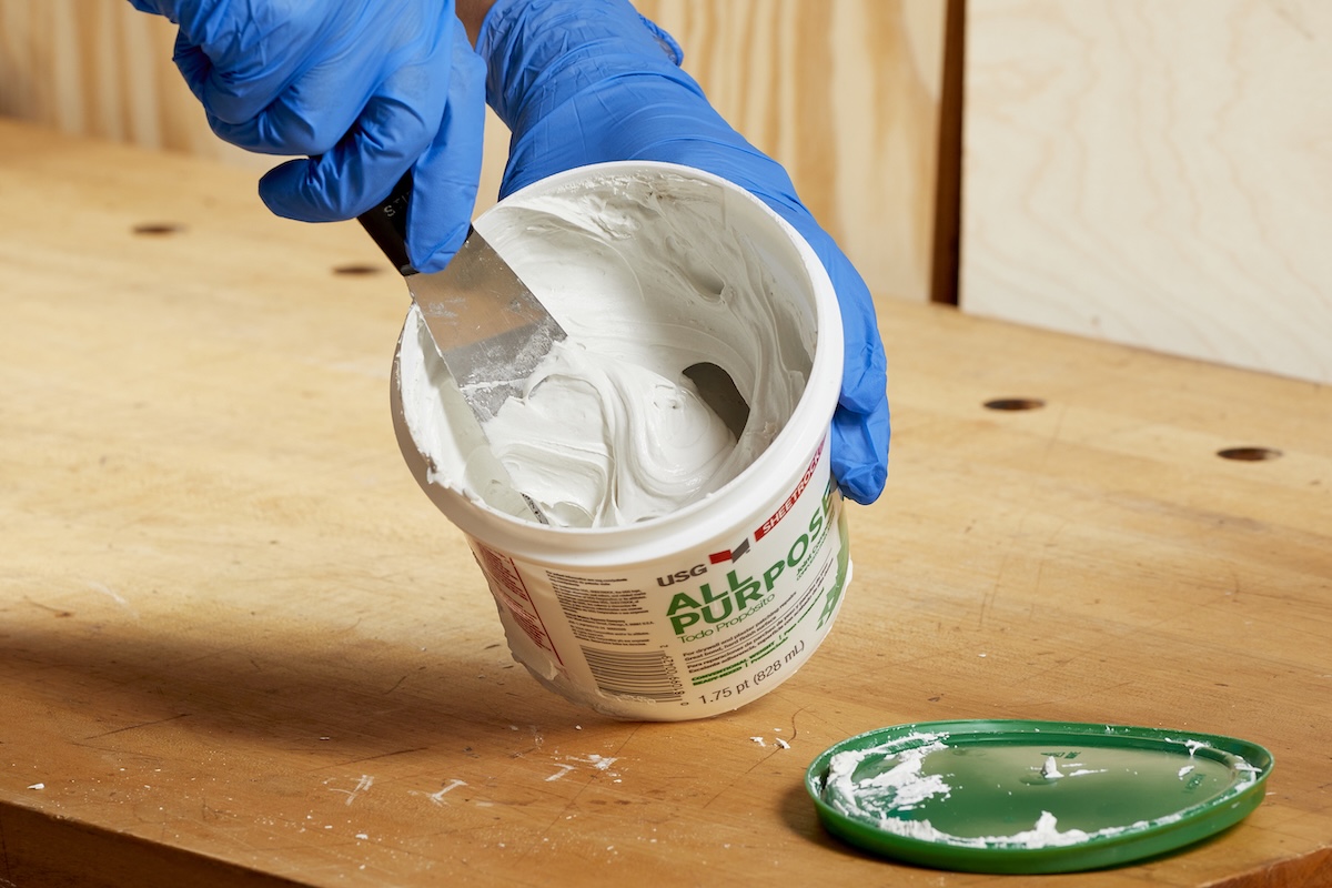 Person wearing nitrile gloves scoops some joint compound out of the container.