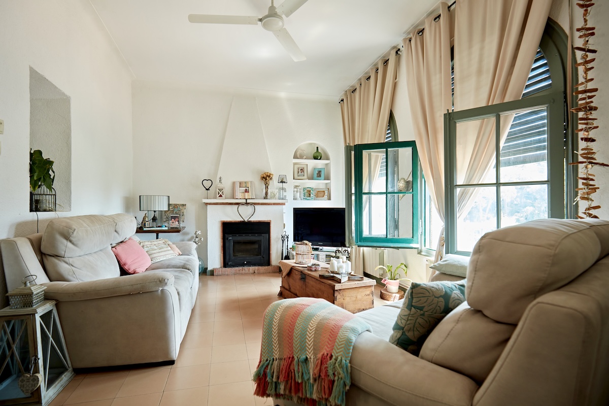 Cozy living room in neutral colors with sofa, loveseat, fireplace, and draperies with a ceiling fan overhead.