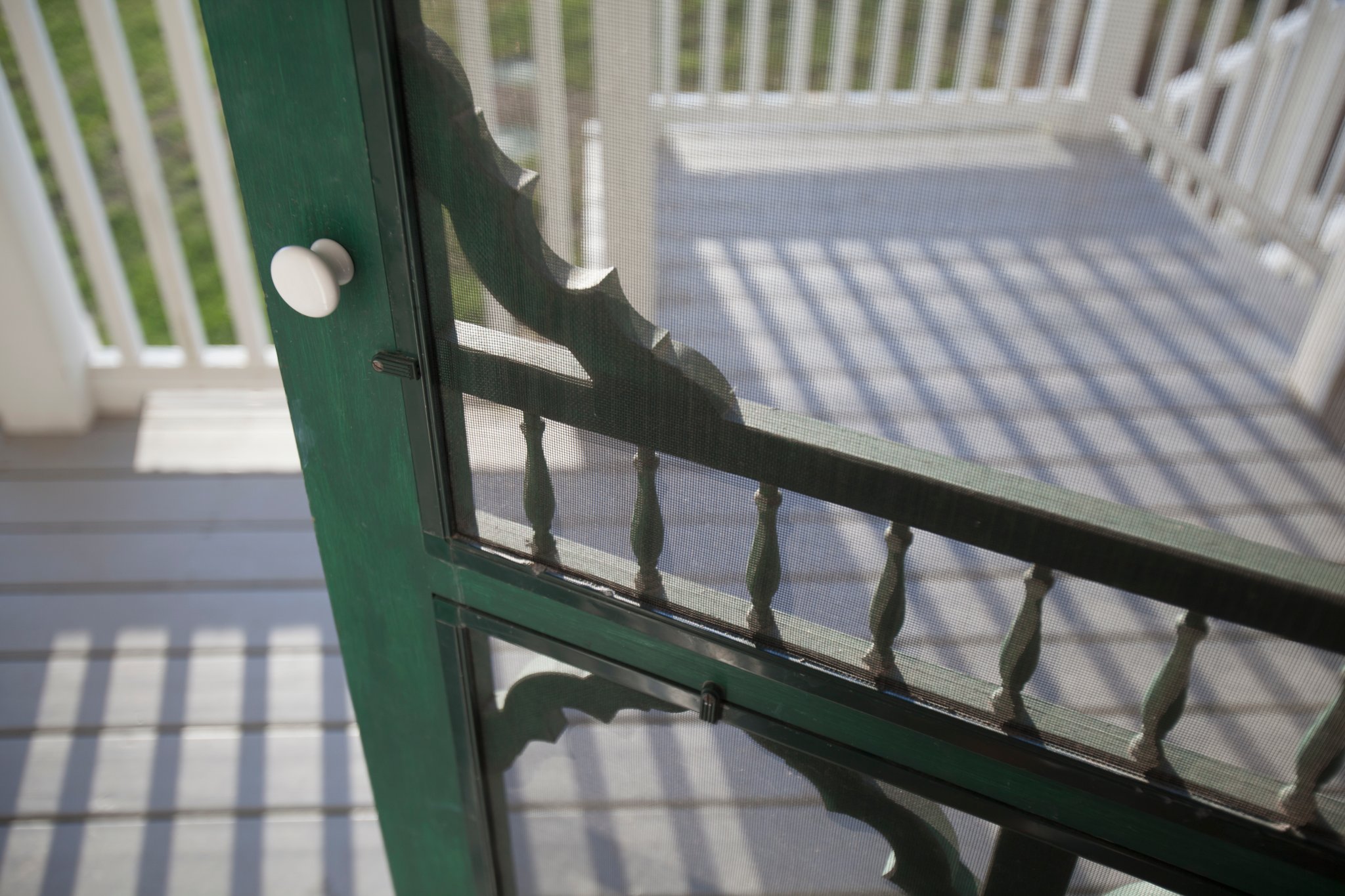 Screen door with green wood trim opens onto a beautiful porch.