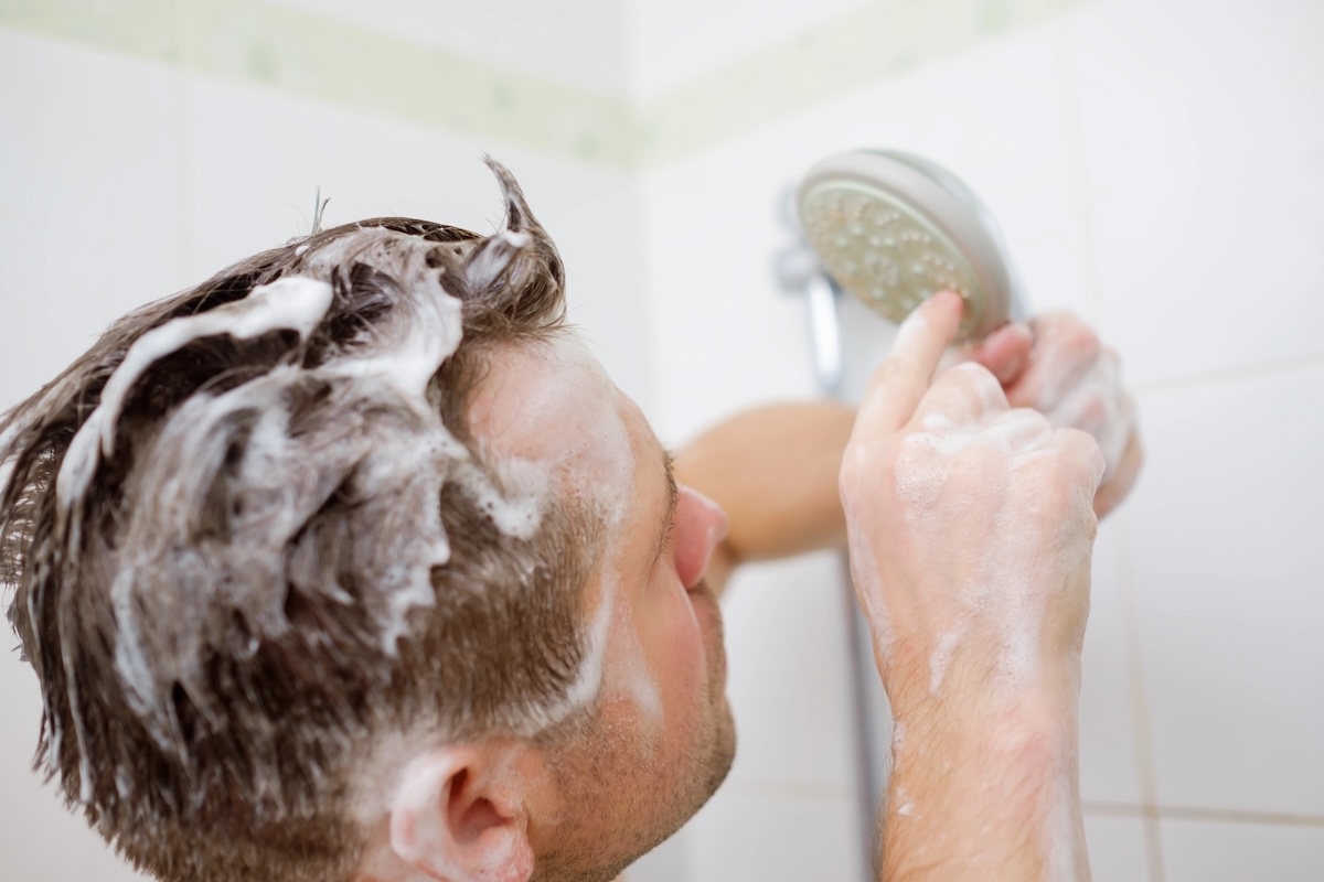 A man with shampoo in his hair attempts to repair a broken shower head.
