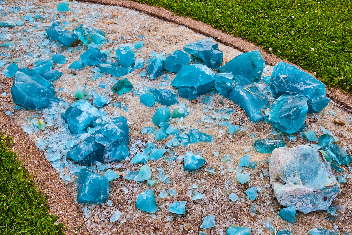 Clear glass fragments and turquoise blue shards lie on a rocky garden pathway.
