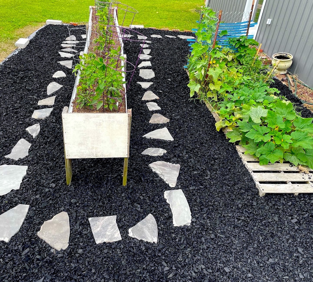 Black rubber mulch is laid around raised and elevated garden beds, with stepping stones throughout.