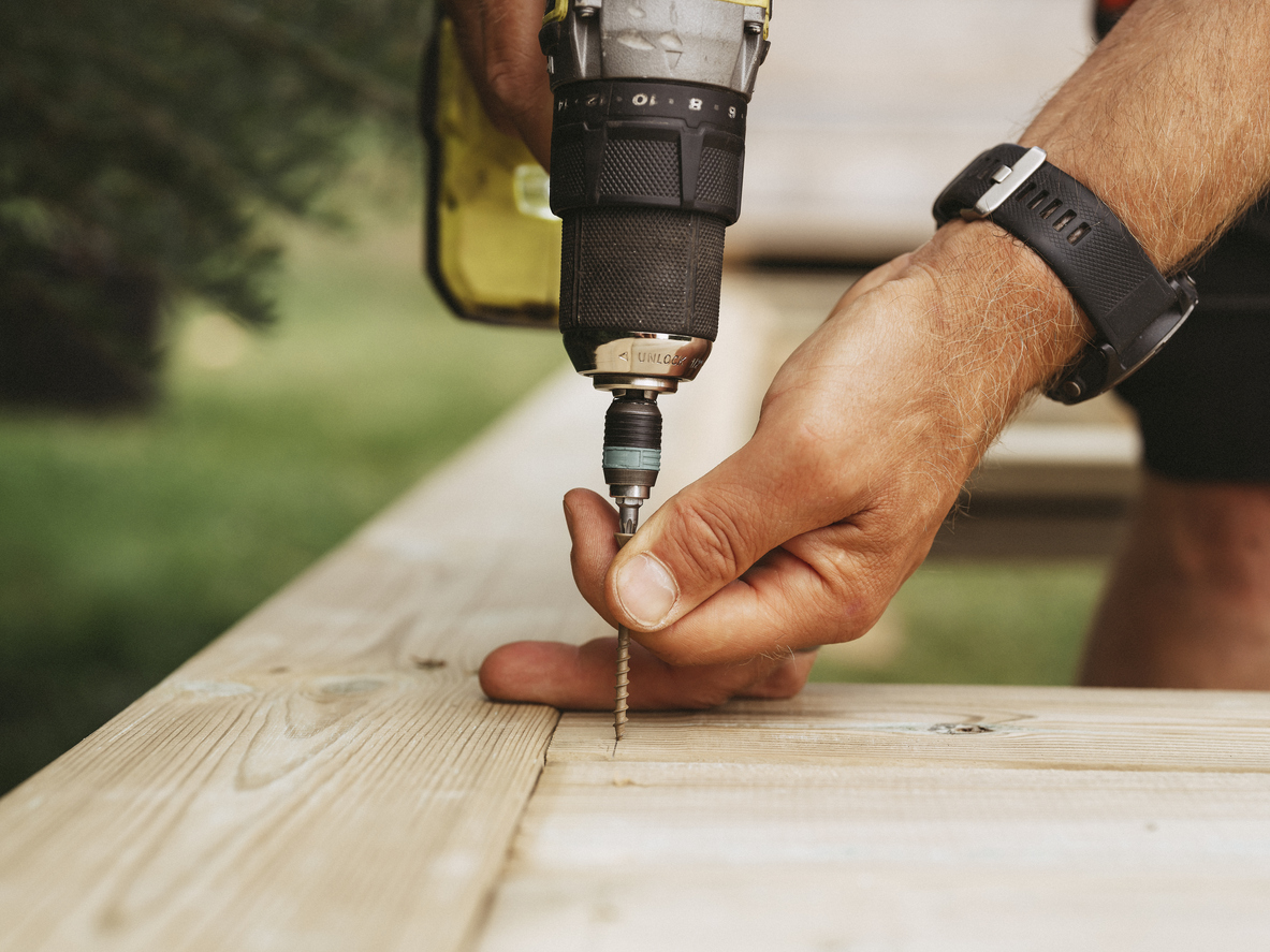 Screwdriver and man building a wooden patio deck outdoors in his garden
