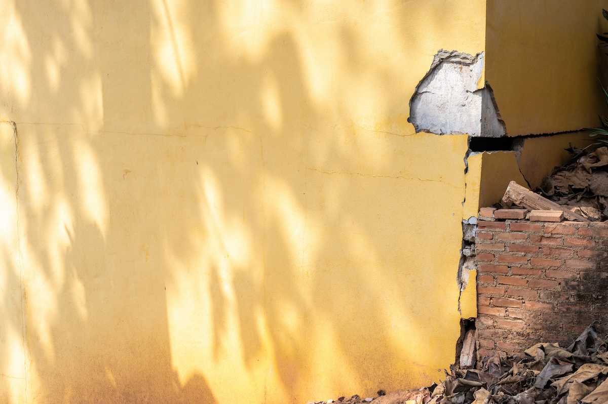 The foundation of a yellow stucco home has a large crack and dent, causing serious damages.