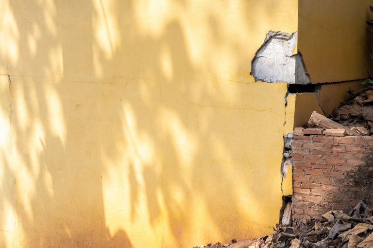 The foundation of a yellow stucco home has a large crack and dent, causing serious damages.