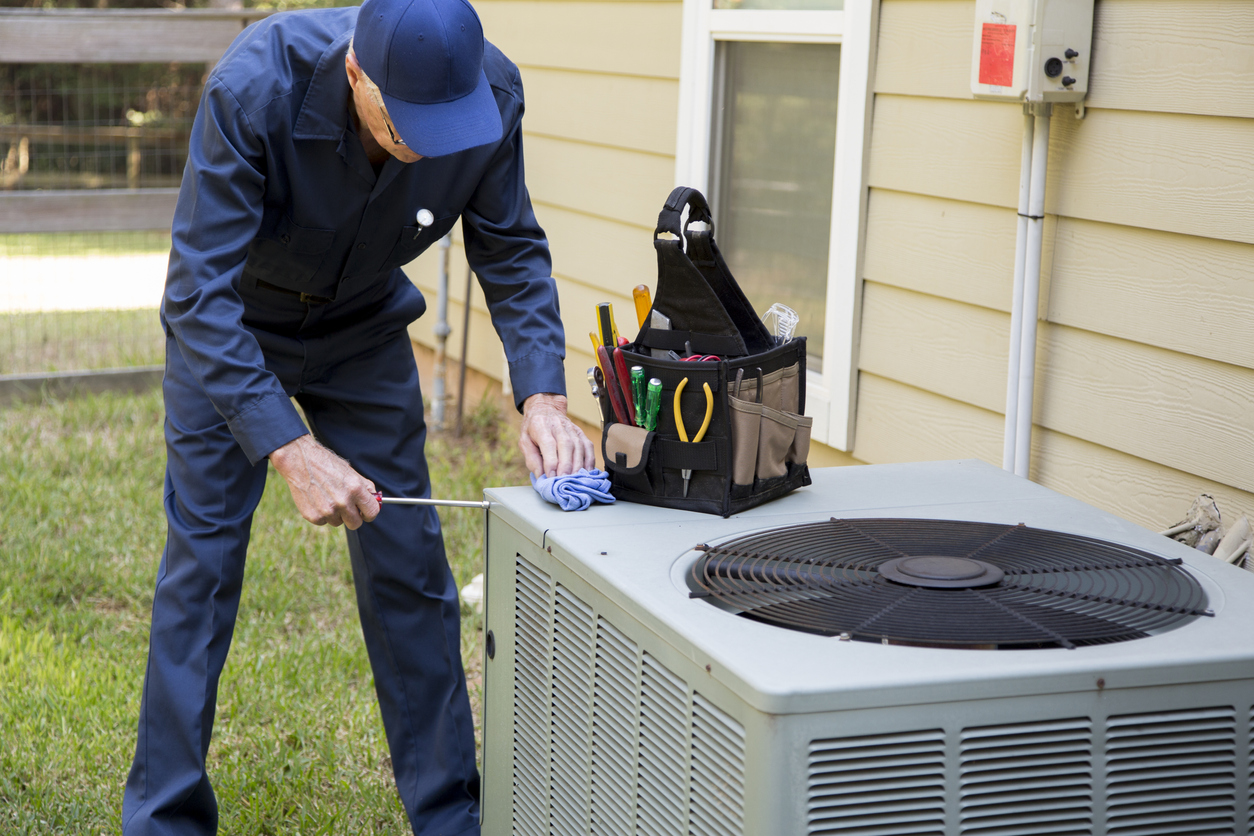 Repairman dressed in blue coveralls replaces dated outdoor air conditioning unit.