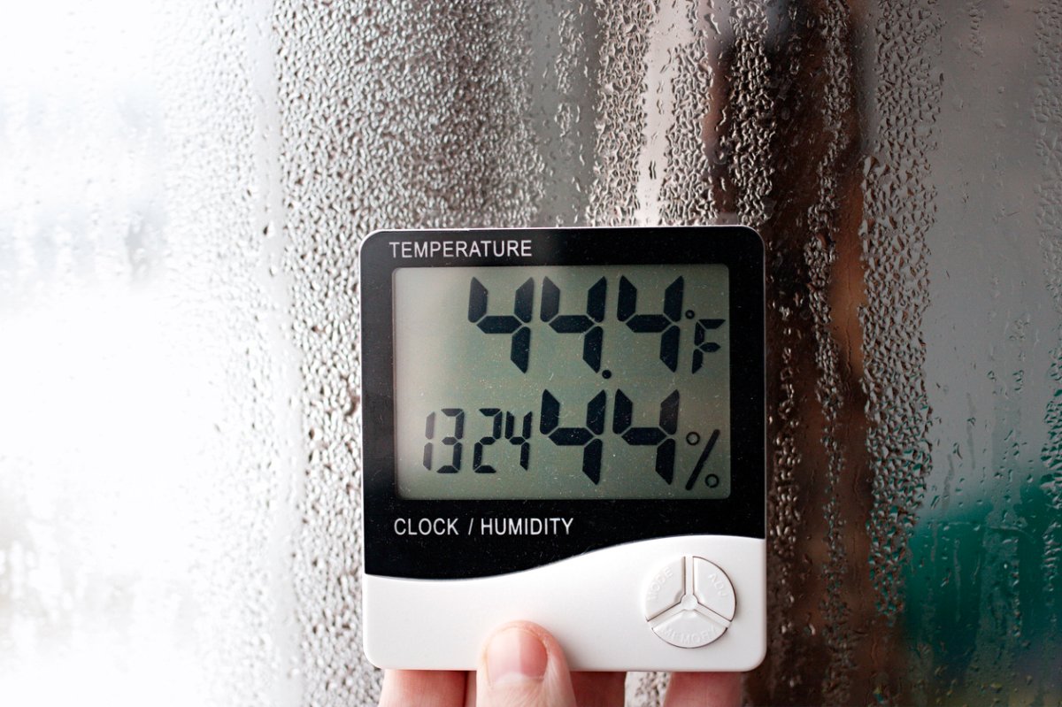 Electric humidity meter held up near window with condensation measures moisture in air.
