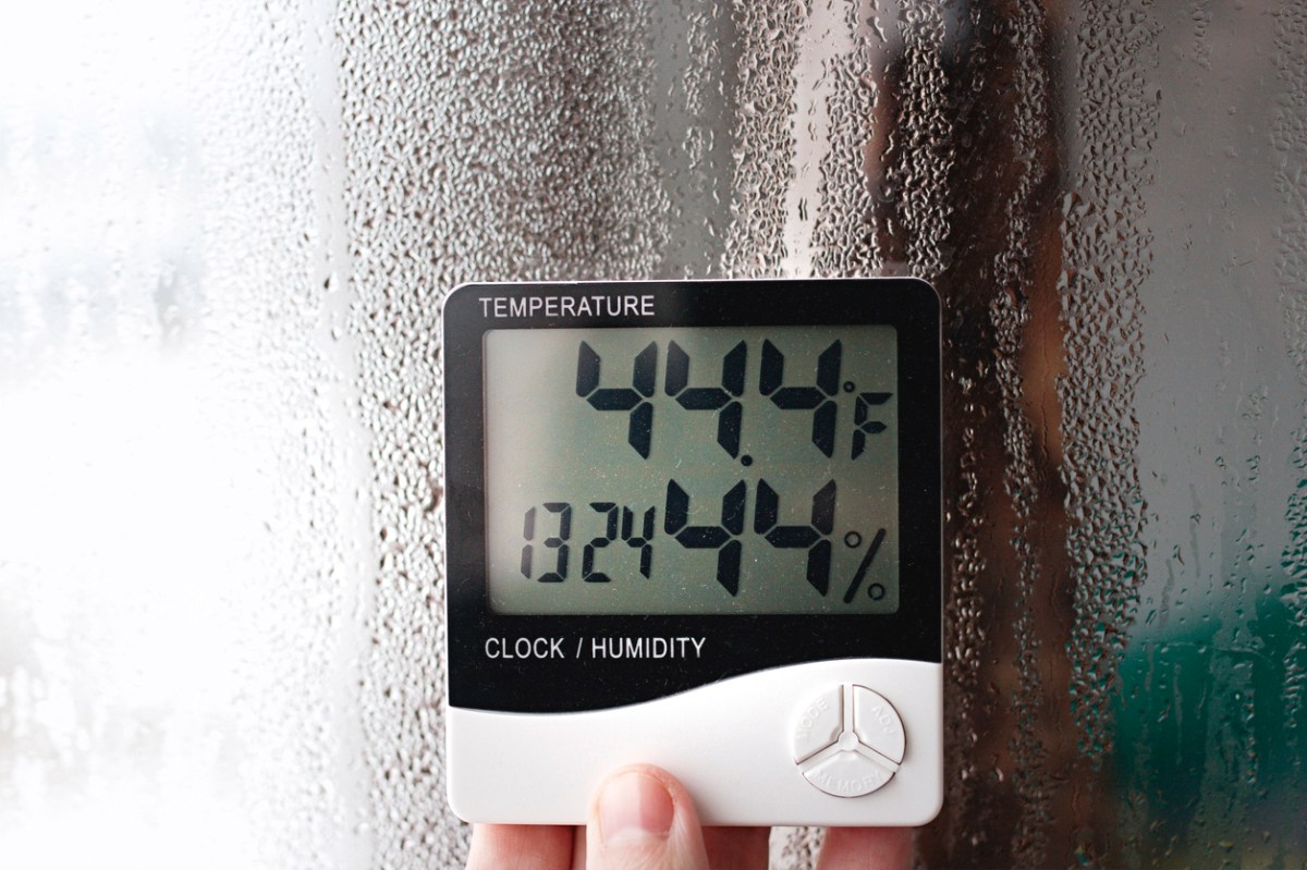 Electric humidity meter held up near window with condensation measures moisture in air.
