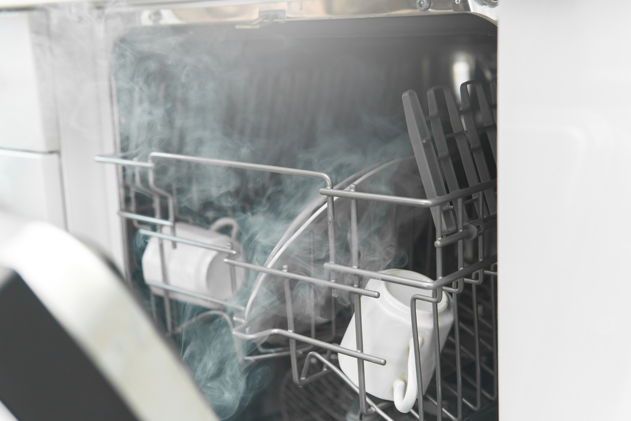 Steam releases from silver dishwasher with ceramic cups inside.