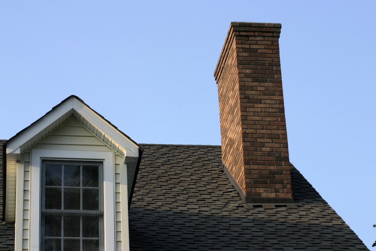 A chimney leans awkwardly on the roof of a house.