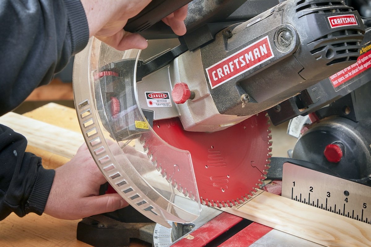 A person uses a red Craftsman miter saw to cut a bevel.