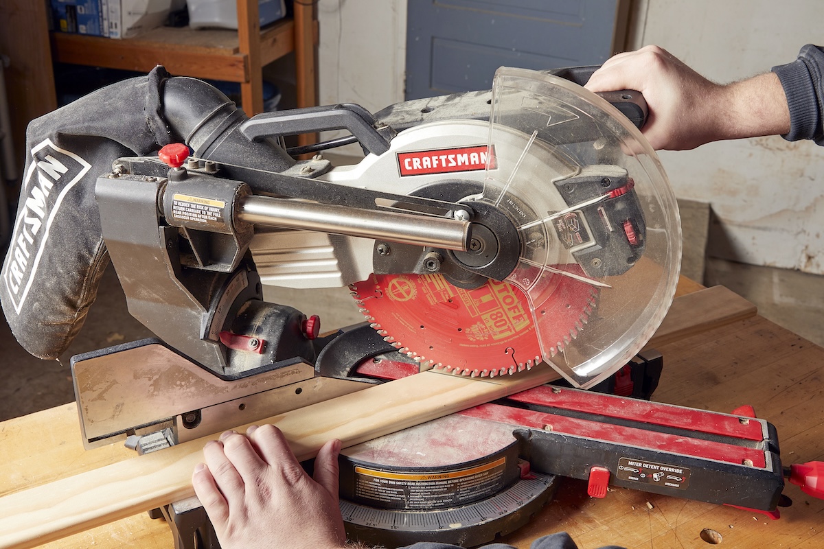 A person uses a red Craftsman-brand miter saw on a wooden workbench.