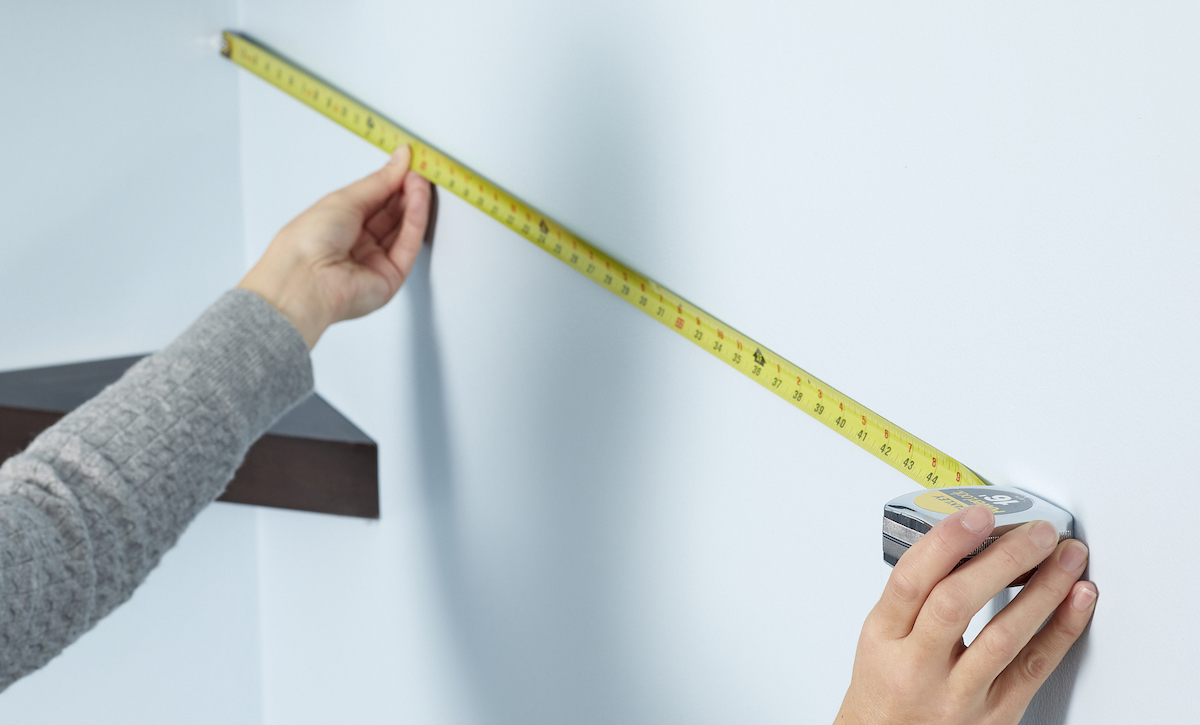 Woman uses a measuring tape to measure wall from corner.